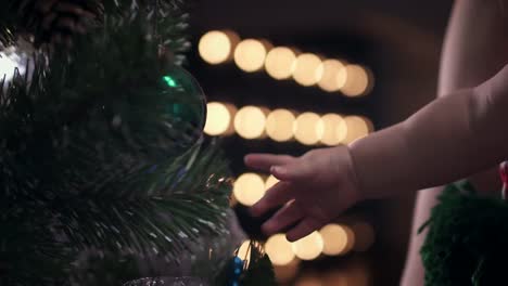 Cute-baby-boy-in-striped-cap-shoots-a-green-ball-toy-from-a-Christmas-tree.-Close-up