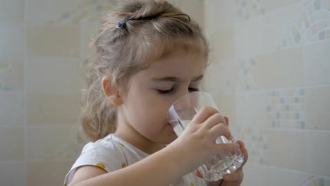 Cute-little-child-girl-drinking-a-glass-water-at-home.