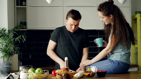 Glückliches-junges-Paar-Kochen-und-plaudern,-während-glücklich-Mann-Schneiden-von-Gemüse-zum-Frühstück-in-der-Küche-zu-Hause.-Beziehung-und-Familie-Konzept