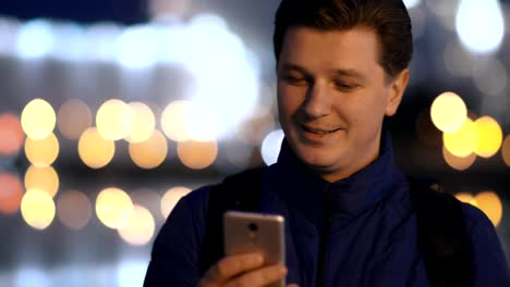 Un-hombre-atractivo-joven-utiliza-un-teléfono-móvil-en-una-ciudad-de-noche.