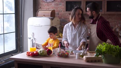 niño-pequeño-con-tableta-digital-mientras-que-los-padres-de-cocina