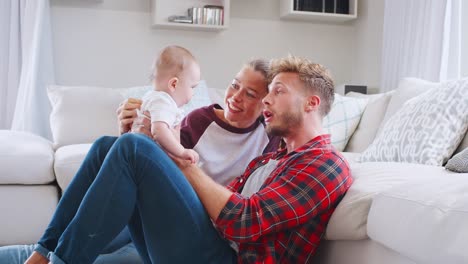 Young-white-couple-sit-playing-with-baby-at-home,-side-view