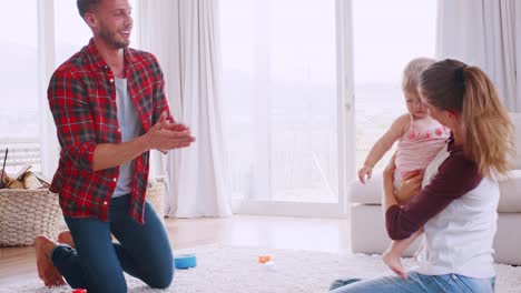 Young-white-couple-teaching-daughter-to-walk-at-home