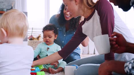 Freunde-mit-Kleinkindern-spielen-auf-dem-Boden-im-Wohnzimmer