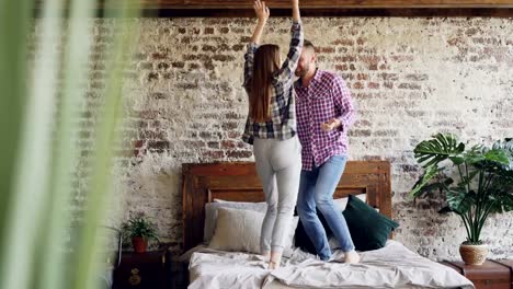 Young-beautiful-and-loving-couple-is-dancing-on-bed-at-home,-careless-people-are-having-fun-and-laughing.-Carelessness,-free-time-and-relationship-concept.