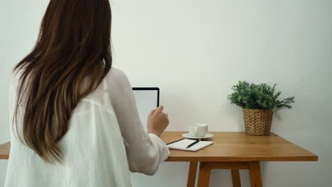 Beautiful-young-smiling-woman-working-on-laptop-while-enjoying-drinking-warm-coffee-sitting-in-a-living-room-at-home.-Enjoying-time-at-home.-Asian-business-woman-working-in-her-home-office.