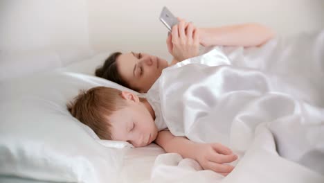 Mamá-se-despertó-y-navegar-por-internet-en-su-teléfono-móvil-mientras-su-hijo-está-todavía-dormido.