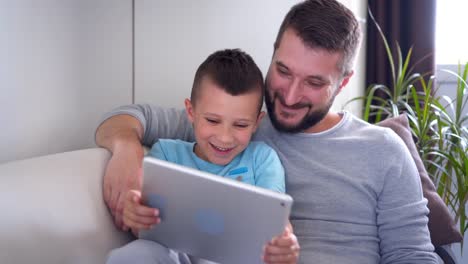 Smiling-father-and-son-using-tablet-while-sitting-on-sofa