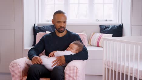 Stressed-New-Father-Sitting-In-Chair-Holding-Sleeping-Baby-Girl-In-Nursery-At-Home