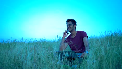 Indischen-Mann-in-der-Brille-Spaß-Kommunikation-am-Telefon-sitzen-auf-dem-Rasen-auf-dem-Hügel-am-Abend