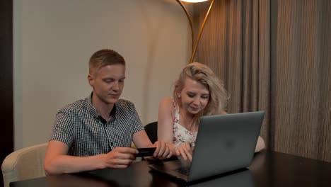 Attractive-Guy-and-girl-sit-on-the-coucand-shop-online-with-credit-card-on-the-laptop-notebook