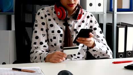 woman-with-red-headphones-on-shoulders-holding-credit-card-and-using-smartphone