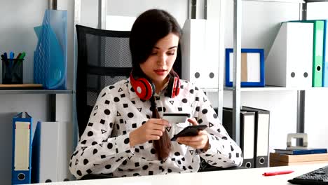 woman-with-red-headphones-on-shoulders-entering-credit-card-number-into-smartphone