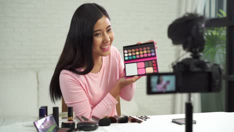 Beauty-blogger-present-beauty-cosmetics-while-sitting-in-front-camera-for-recording-video.-Beautiful-woman-use-brush-while-review-make-up-tutorial-broadcast-live-video-to-social-network-by-internet.