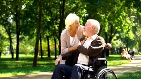 Mature-wife-taking-care-of-her-beloved-husband-in-wheelchair,-happy-marriage