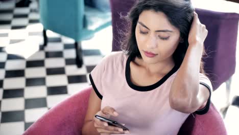 Un-tiro-de-movimiento-de-las-sonrisas-de-mujer-joven-durante-el-uso-de-teléfono-móvil-en-una-cafetería-moderna.