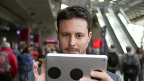 Handsome-young-businessman-writing-texts-on-digital-tablet-in-public-space