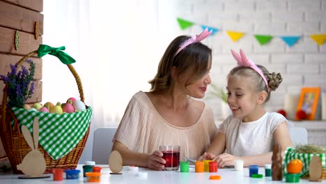 Cute-daughter-dipping-egg-into-glass-with-red-food-coloring,-Easter-traditions