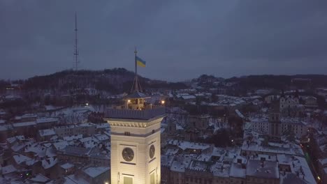 LEMBERG,-UKRAINE.-Panorama-der-antiken-Stadt.-Kamera-bewegt-sich-in-der-Nähe-der-ukrainischen-Flagge.-Ukraine-Lviv-Stadtrat,-Rathaus.-Die-Dächer-von-Altbauten.-Antenne,-Ansicht-der-Drohne.-Winternacht