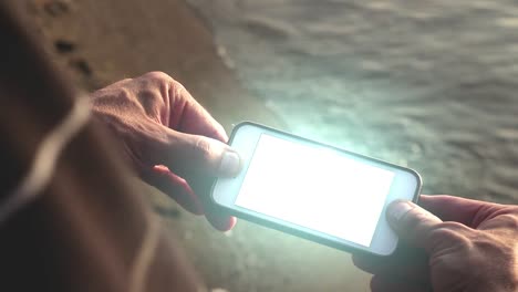 Glowing-futuristic-smartphone-being-held-by-man-on-beach---Tech-Concept