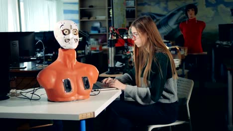 Upper-half-of-a-cyborg's-body-and-a-young-woman-operating-a-laptop