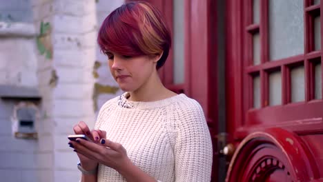 Retrato-de-joven-caucásico-rosa-chica-de-pelo-alegre-trabajando-con-el-teléfono-inteligente-en-el-fondo-de-la-puerta-roja.