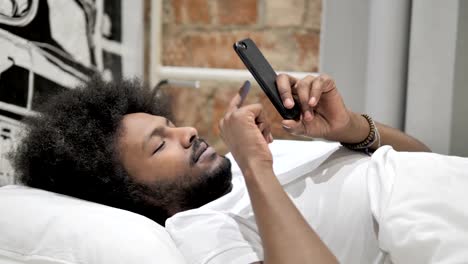 Hombre-africano-usando-smartphone,-acostado-en-la-cama