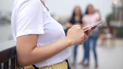 Junge-asiatische-Frau-mit-Smartphone-im-Freien-öffentlichen-Park.-Slow-Motion-hautnah.-Suche-im-Internet,-Online-Technologie.