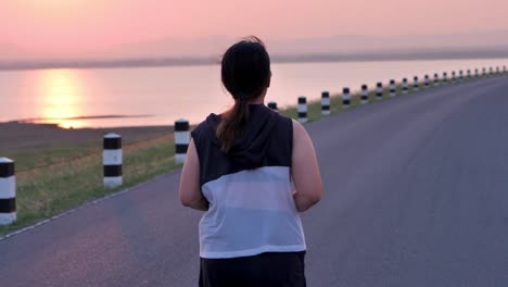 Übergewichtige-asiatische-Frauen-joggen-am-frühen-Morgen-im-Sonnenlicht-auf-der-Straße.-Konzept-des-Gewichtsverlustes-mit-Bewegung-für-die-Gesundheit.-Langsame-Bewegung,-Rückansicht