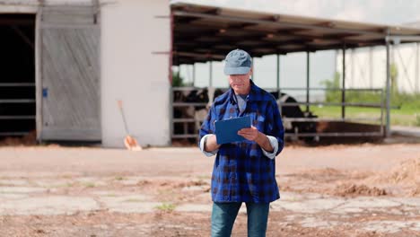 Landwirtschaft.-Landwirt-mit-digitalem-Tablet-beim-Betrachten-von-Kühen