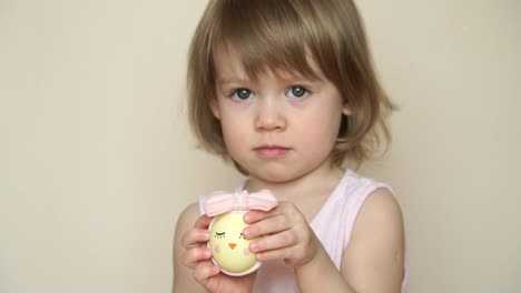 Portrait-of-little-pretty-smiling-caucasian-girl-holds-in-hand-chicken-egg-decorated-for-Easter-chick,-with-painted-muzzle-with-eyes.