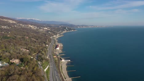 Toma-de-video-aéreo.-La-costa-del-mar-negro-de-Sochi-desde-una-altura.-La-cámara-se-mueve-desde-la-orilla.-costa.-La-carretera-a-lo-largo-de-la-orilla-del-mar.-Montañas-de-Krasnaya-Polyana.