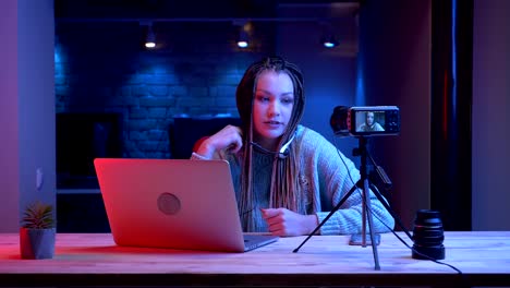 Closeup-shoot-of-young-attractive-female-blogger-with-dreadlocks-in-headphones-playing-video-games-with-the-neon-background-indoors