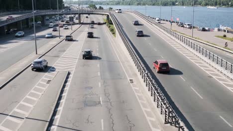 Aerial-view-from-Metro-Bridge,-also-known-as-Mostmetro,-heavy-traffic-in-the-day,-Dnipro-river-and-city-skyline.-Big-city-life-concept.-Ukraine,-Kyiv,-01.06.2019