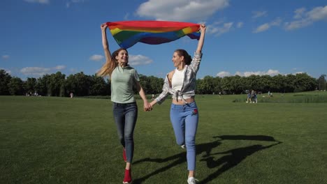 Lesbianas-felices-con-bandera-arco-iris-corriendo-en-el-parque