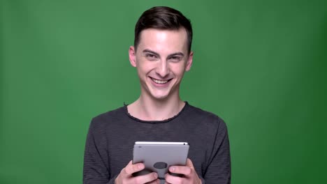 Closeup-shoot-of-young-handsome-caucasian-male-using-the-tablet-looking-at-camera-and-smiling-with-background-isolated-on-green