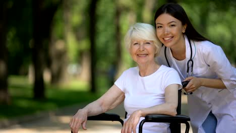 Nurse-and-elderly-woman-in-wheelchair-smiling-at-camera-and-showing-thumbs-up