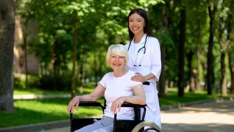 Female-nurse-and-disabled-aged-woman-smiling-to-camera,-relax-in-hospital-park