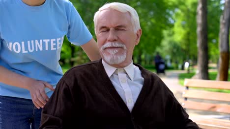 Young-female-volunteer-walking-in-hospital-garden-with-old-man-in-wheelchair