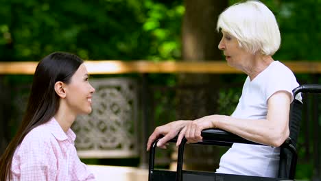 Mujer-sonriente-voluntaria-hablando-con-una-anciana-en-silla-de-ruedas,-apoyo