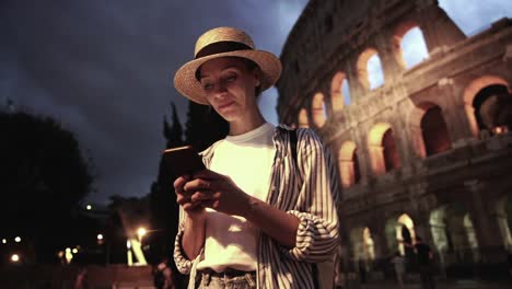 Alegre-viaje-femenino-milenario-caucásico-leer-mensaje-en-el-teléfono-inteligente-conectado-a-4G-en-itinerancia-mientras-disfruta-de-viaje-a-Roma-por-la-noche