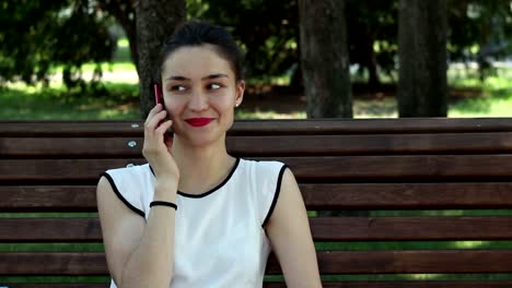 Young-beautiful-girl-talking-on-the-phone-while-sitting-on-a-park-bench.