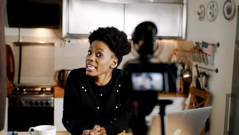 Happy-young-professional-African-female-fashion-blogger-filming-video-blog-using-camera-at-home-kitchen-slow-motion.