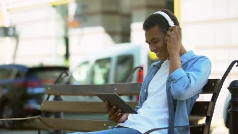 Cheerful-mixed-race-boy-with-tablet-putting-off-earphones-smiling-to-camera