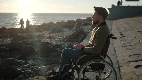 Lonely-disabled-man-with-mobile-near-the-sea