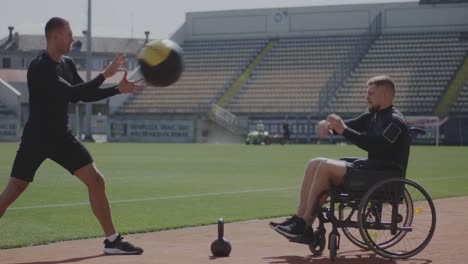 Atleta-en-silla-de-ruedas-y-entrenador-lanzando-pelota-de-medicina