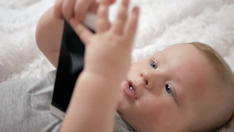 Lindo-bebé-sostiene-el-teléfono-en-las-manos.-El-niño-juega-con-el-teléfono-celular,-lo-examina,-tira-en-sus-manos-y-trata-de-comer-teléfono-inteligente-poniéndolo-en-su-boca