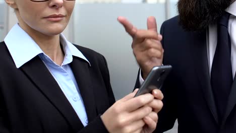 Empresario-en-traje-regañando-mujer-secretaria-desplazamiento-teléfono-al-aire-libre,-fecha-límite