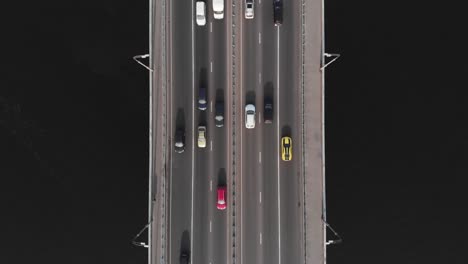 Bridge-highway-dark-water-red-yellow-cars-in-traffic-aerial-top-view