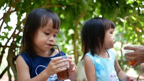 Little-Asian-child-girl-sipping-her-drink-while-sitting-rest-in-the-park-on-summer-day.-Selective-focus.